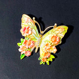 Butterfly-shaped enamel metal brooch with peach and green floral design on a blue background