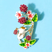 Brooch with a harvest mouse, berries, and flowers on a blue background