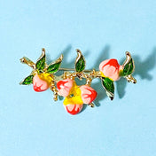 peach fruits with green leaves enamel and gold tone metal brooch on a blue background