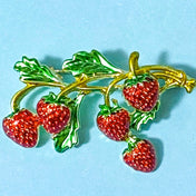 Strawberry brooch with gold stem and green leaves on a blue background