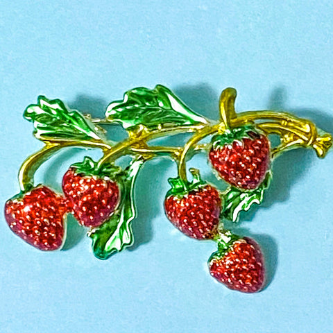Strawberry brooch with gold stem and green leaves on a blue background