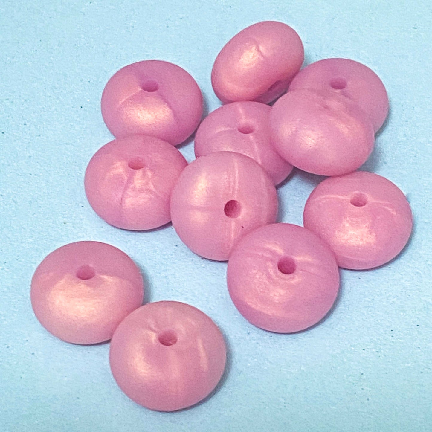 silicone spacer beads with a chunky shape in pearlescent pink on blue background