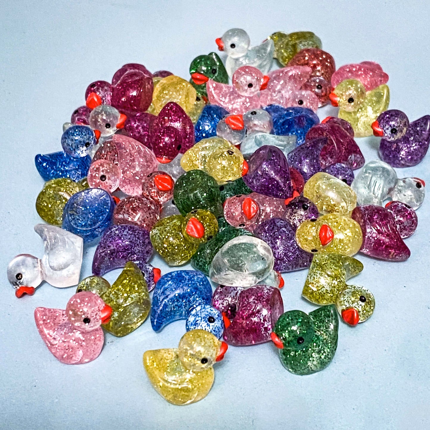 Colorful glittery duck-shaped figurines on a light blue background