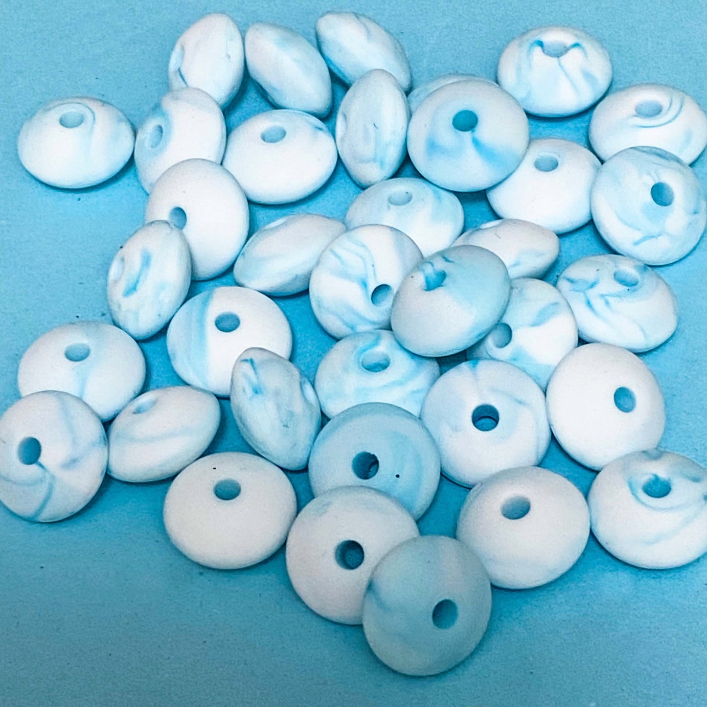 marbled light turquoise and white silicone spacer beads on a blue background