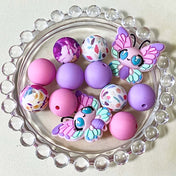 pastel silicone bead bundle with butterfly feature bead, pink and lilac round beads and floral patterned beads on a round glass plate