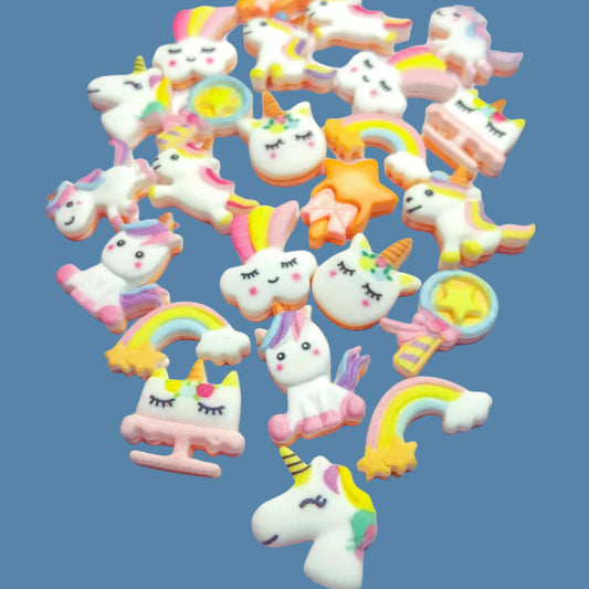 A collection of pastel-colored resin flatbacks featuring designs of unicorns, magic wands, clouds, rainbows, and a unicorn cake.